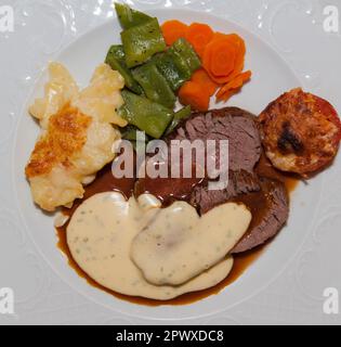 Gros plan d'un plat principal allemand typique avec des tranches de rôti, des légumes partiellement gratinés, de la sauce et du gratin de pommes de terre Banque D'Images