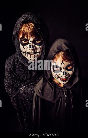 Deux enfants portent des robes sombres et de la peinture effrayante pour le visage à Halloween. Banque D'Images