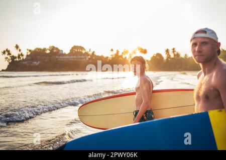 Un jeune garçon avec une planche de surf va à la mer de surf. Il a des vacances d'hiver et profiter d'un beau coucher de soleil avec son père sur l'île du Sri Lanka. Banque D'Images