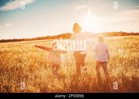 Mère avec ses enfants en train de courir sur le terrain au coucher du soleil d'été. Concept de la relation familiale et des vacances. Banque D'Images