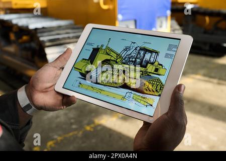 Gros plan de la tablette avec photo de bulldozer à l'écran tenu par un jeune ingénieur afro-américain ou constructeur de machines industrielles Banque D'Images