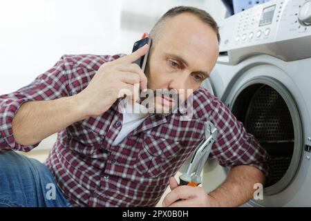 homme parlant sur téléphone portable tout en mettant la lessive Banque D'Images