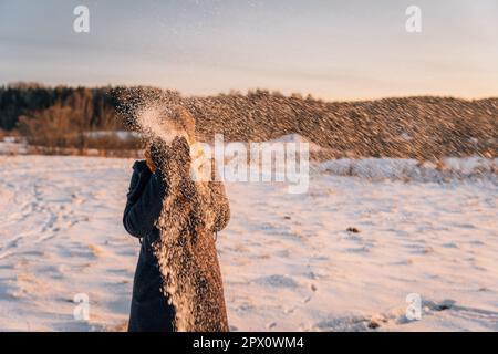 Une femme non identifiée jette de la neige dans un champ couvert de neige. Banque D'Images