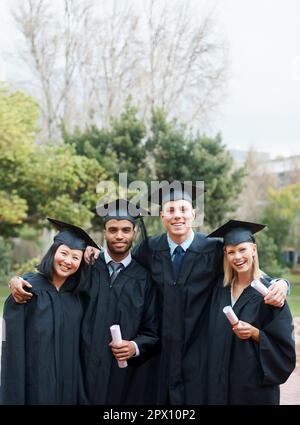 La yve a forgé des obligations à vie. Un groupe de diplômés de collège debout en chapeau et en robe et portant leurs diplômes. Banque D'Images