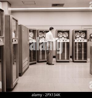 1960S HOMME TECHNICIEN INFORMATIQUE DEBOUT DEVANT UN ENSEMBLE D'UNITÉS DE STOCKAGE DE DONNÉES SUR BANDE MAGNÉTIQUE IBM MODÈLE 727 - O2052 HAR001 TECHNICIEN HARS HOMMES PROFESSION 1953 DONNÉES B&W COMPÉTENCES GRAND ANGLE AVANT PROFESSION COMPÉTENCES TÔT RÉSEAUTAGE CARRIÈRES PUISSANTE ORIENTATION DE PROGRÈS INNOVATION TRAVAIL UNE DES PROFESSIONS DE L'EMPLOI CONNEXION CONCEPTUELLE ÉLÉGANT SOUTIEN STIMULE LA CROISSANCE DES EMPLOYÉS DE L'INFRASTRUCTURE MOYENNE-ADULTE MI-ADULTE HOMME DE PRÉCISION SYSTÈMES ARRAY RACE BLANCHE ET NOIRE ERA HAR001 LALABEUR MAGNÉTIQUE ANCIEN MODE Banque D'Images