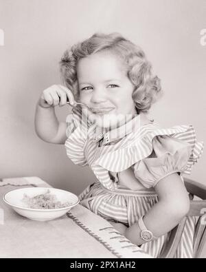 1940S MIGNONNE SOURIRE PETITE FILLE EN ROBE FANTAISIE REGARDANT L'APPAREIL PHOTO MANGER DES CÉRÉALES PETIT DÉJEUNER - F2242 HAR001 HARS MI-LONGUEUR FANTAISIE RAYURES CONFIANCE B&W CONTACT VISUEL BONHEUR BIEN-ÊTRE NUTRITION CONSOMMER NOURRITURE CONSOMMER NOURRITURE ÉLÉGANT PINAFORE AGRÉABLE AGRÉABLE COOPÉRATION CHARMANTE CROISSANCE JEUNES ADORABLES AGRÉABLE ADORABLE ET ATTRAYANT NOIR ET BLANC DE RACE BLANCHE HAR001 OLD FASHIONED Banque D'Images