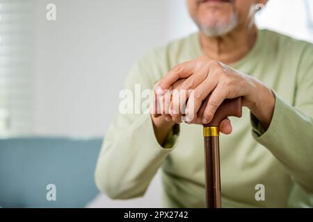 Les mains de l'asiatique Old man assis à la maison tiennent la canne à pied en bois, les personnes âgées main tenant la poignée de la canne, l'homme handicapé senior tenant la stic de marche Banque D'Images