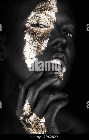 Portrait de mode d'une fille à la peau sombre avec maquillage d'or.visage de beauté. Photo prise en studio sur fond noir. Banque D'Images