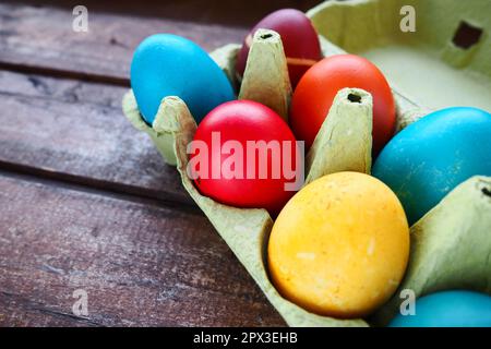 Œufs multicolores peints avec gouache et pelure d'oignon dans une boîte en carton sur fond de table en bois. Dix œufs durs. Affiche de carte postale pour Pâques. E Banque D'Images