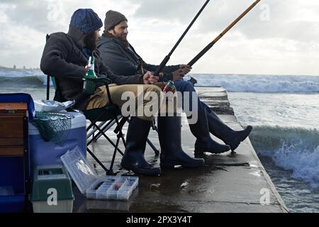 Traîner, juste attraper un peu de poisson. deux jeunes hommes pêchant à la plage le matin. Banque D'Images