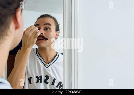 Reflet d'une personne blanche non binaire d'origine latino-Argentine, à l'intérieur de sa chambre, appliquant du maquillage à ses paupières, concept de beauté, espace de copie Banque D'Images