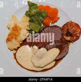 Gros plan d'un plat principal allemand typique avec des tranches de rôti, des légumes partiellement gratinés, de la sauce et du gratin de pommes de terre Banque D'Images