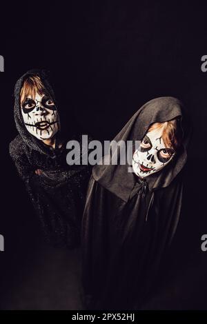 Deux enfants portent des robes sombres et de la peinture effrayante pour le visage à Halloween. Banque D'Images