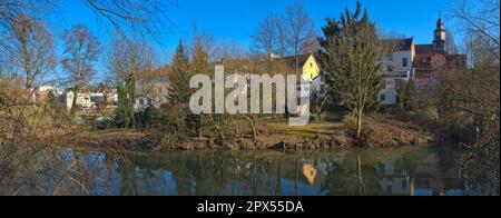 La rive de la Nidda dans un vieux centre de village de Francfort-sur-le-main avec des jardins, des plantes au bord de la rivière, des arbres, des maisons résidentielles et une tour d'église Banque D'Images