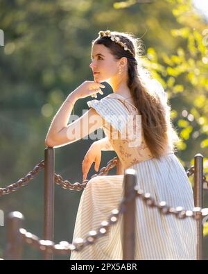 Jeune femme portant la robe de base de Cottage debout sur un pont avec la main sur Chin regardant de rêve hors de la caméra Banque D'Images