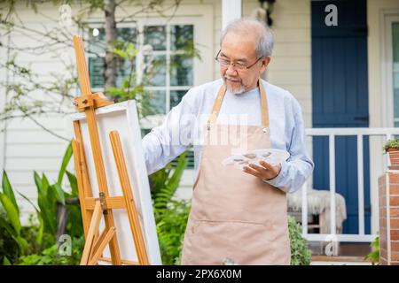 Style de vie asiatique senior homme de la peinture de l'art d'image en utilisant la couleur de pinceau et d'huile sur la toile, les personnes âgées sourient la peinture à son chevalet à l'extérieur vert nat Banque D'Images