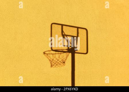 L'ombre d'un panier de basket-ball est silhouetée contre le mur jaune d'une maison près du soleil Banque D'Images