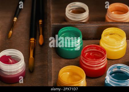 Gouache artistique et pinceaux en boîte de chevalet en bois, tir grand angle. Huit bouteilles ouvertes de peintures à la gouache et trois pinceaux dans une boîte de chevalet Banque D'Images