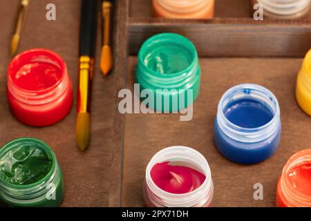 Neuf bouteilles ouvertes de peintures à la gouache et trois pinceaux en boîte de chevalet, grenaille à grand angle Banque D'Images