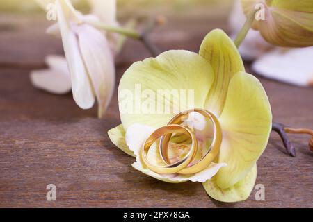 Anneaux de mariage dorés sur une orchidée jaune sur une table en bois. Cérémonie de mariage, lune de miel, proposition de mariage, la Saint-Valentin dans les pays chauds. Copier l'espace Banque D'Images