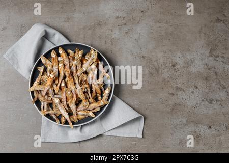 Assiette d'anchois séchés savoureux et serviette sur table grise, vue de dessus. Espace pour le texte Banque D'Images