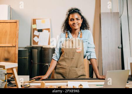 Portrait de l'afrique américaine beau jeune femme noire charpentier portant des lunettes de protection sur la tête debout sur la table d'espace de travail à l'atelier contre W Banque D'Images