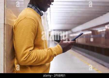 Homme afro-américain communiquant en ligne sur smartphone en attendant le train en métro Banque D'Images