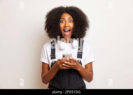 Une femme aux cheveux mauriques a eu le message sur le smartphone, a ouvert ses yeux et la bouche dans une énorme surprise, isolée à côté du mur blanc. Banque D'Images