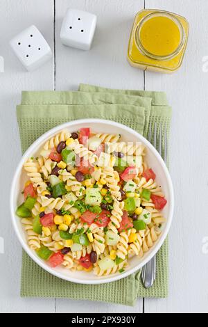 Salade de pâtes vegan fusilli fraîches et colorées faites maison avec haricots, maïs, tomate, concombre et poivron vert servi dans un bol, vinaigrette sur le Banque D'Images