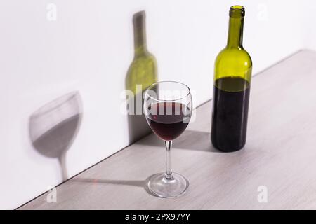 Un verre de vin et une bouteille jettent une longue ombre du soleil du soir. Banque D'Images