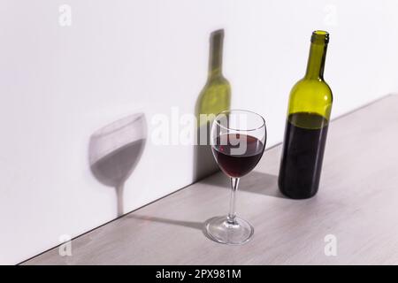 Un verre de vin et une bouteille jettent une longue ombre du soleil du soir. Banque D'Images