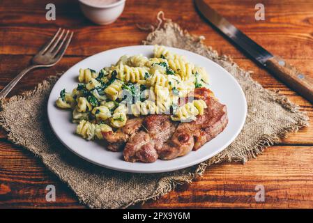 Steak de porc et pâtes crémeuses aux épinards et au thym Garni de parmesan râpé sur plaque blanche Banque D'Images