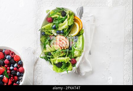 Salade verte saine avec fruits aux baies et aux pommes sur fond blanc. Salade fraîche avec ingrédients de fruits et légumes verts. Une alimentation saine. Banque D'Images