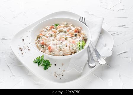 Assiette de salade russe ou de salade française avec légumes et œufs vêtus de mayonnaise sur table blanche Banque D'Images