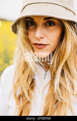 Belle jeune femme blonde, portant un chapeau, pose au milieu d'un champ de fleurs de colza jaune Banque D'Images