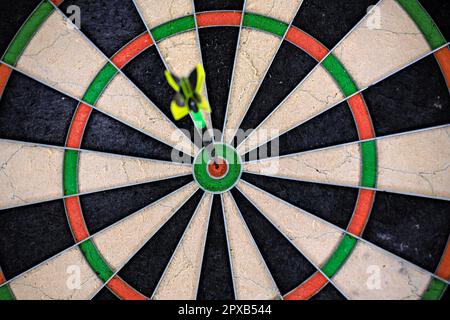 Un seul dart noir et vert collé dans le logo de la cible d'un dartboard. Gros plan sur un plan de travail. Banque D'Images