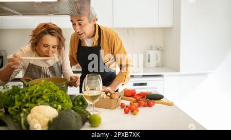 Les conjoints âgés enthousiastes cuisinant ensemble à la maison, repas de dégustation, faire un dîner sain, intérieur de cuisine, espace de copie Banque D'Images