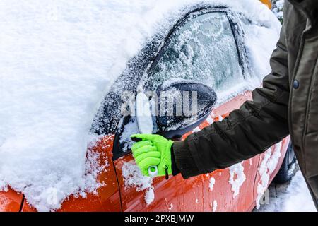 L'adolescent nettoie la voiture après une chute de neige, en enlevant la neige et en raclant la glace Banque D'Images