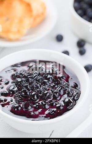 Confiture maison fraîche faite de baies de Calafate de Patagonie (lat. Berberis heterophylla), servie dans un bol blanc, pain grillé et baies crues à l'arrière ( Banque D'Images