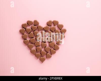 Grand coeur fait de confiseries romantiques au chocolat en formes de coeur sur fond rose pastel. Cœur de bonbons pralins au chocolat au lait, espace de copie. Haut vi Banque D'Images