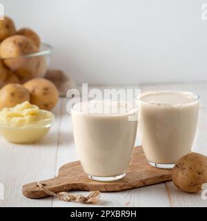 Lait de pomme de terre en verres sur fond blanc en bois. Verser le lait végétalien dans le verre, avec la purée de pommes de terre et les tubercules de pommes de terre sur le fond. Copier l'espace. Ma. Domicile Banque D'Images