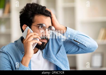 A souligné le jeune Indien Guy en lunettes de vue parlant sur le téléphone cellulaire et touchant la tête Banque D'Images