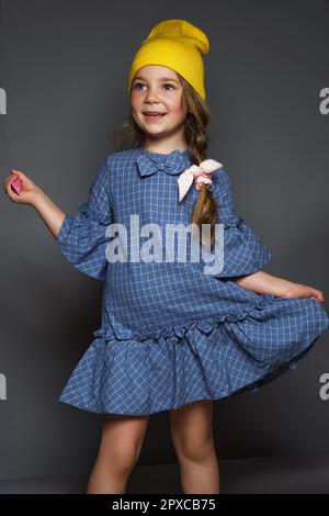 Petite fille modèle professionnellement posant dans le studio dans une robe et un chapeau jaune. Banque D'Images