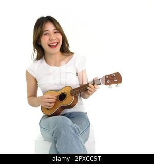 Jeune femme asiatique en t-shirt blanc et jean jouant une guitare Ukulele. Portrait sur fond blanc avec lumière studio. Banque D'Images