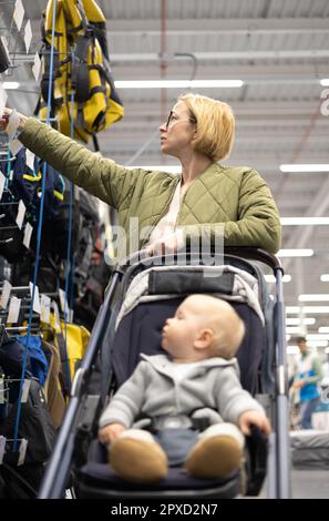 Casualy mère habillée choisissant des chaussures et des vêtements sportifs dans le rayon des sports du magasin de supermarché avec son bébé garçon enfant dans poussette Banque D'Images