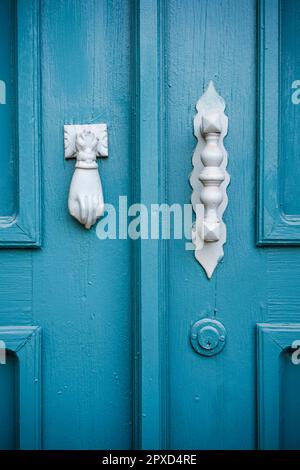 Un porte-outil en forme de main et une poignée en métal sur une ancienne porte peinte en bleu. Banque D'Images