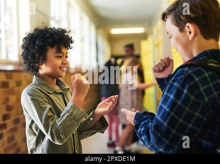 Je vais gagner celui-ci. deux jeunes garçons se tenant ensemble dans le couloir de l'école et jouant un jeu de rock, de papier et de ciseaux. Banque D'Images