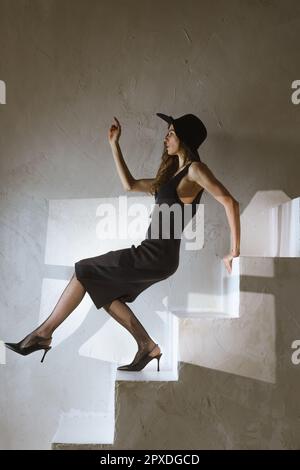 Belle femme est l'équilibre sur des escaliers en béton pour ne pas tomber sur des talons hauts, studio conceptuel tourné avec jeune femme élégante Banque D'Images