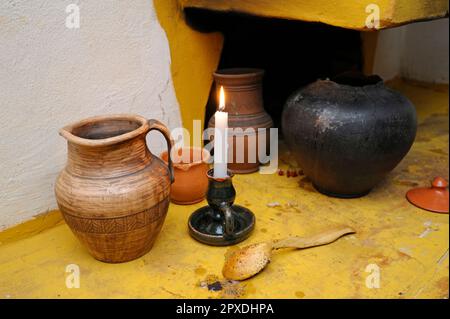 Argile traditionnelle ukrainienne d'égout, pot, cuillère en bois et bougie allumée placée près de vieux four rustique. Kiev, Ukraine Banque D'Images