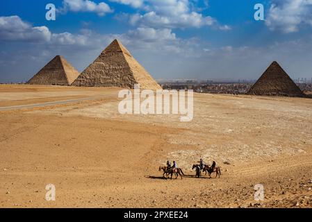 Quatre personnes à cheval sur un vaste paysage désertique, avec les majestueuses pyramides de Gizeh en arrière-plan Banque D'Images